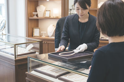 真珠専門店で、白い手袋をした店員がパールネックレスをお客様に見せている様子